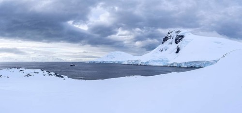 Snow-covered mountain landscape with glacier breakup on the coast, expedition ship anchored in the