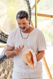 A male sound therapist practices sound therapy, using a conch shell in a serene setting. Observing