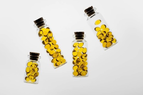 Transparent glass bottles filled with vibrant yellow Omega-3 and vitamin D capsules placed on a