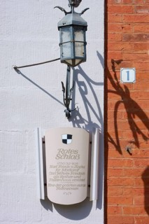 Sign and lantern on a brick wall cast shadows under bright light, Red Castle, Triesdorf,