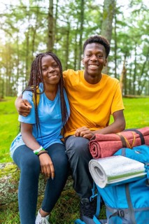 Vertical portrait of two young african friends sitting on fallen tree and resting during hiking