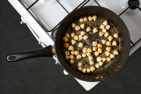 Scallops are being cooked in a frying pan on a stove. The pan is on a gas burner. The kitchen has a