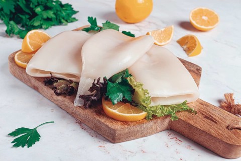 Fresh squid prepared for cooking, surrounded by herbs and lemon, placed on a wooden chopping board