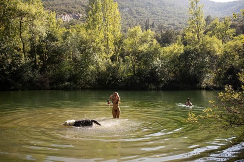 A man and two women enjoy a warm summer day in a serene lake surrounded by lush greenery. One woman