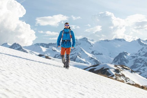 A man, equipped with trekking gear, confidently traverses the snowy slopes of the Pyrenees. The