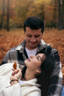 A couple shares a tender moment surrounded by the vibrant colors of autumn leaves in a wooded area.