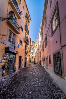 Cobblestoned narrow street lined with colorful buildings under a blue sky, Alfama, Lisbon