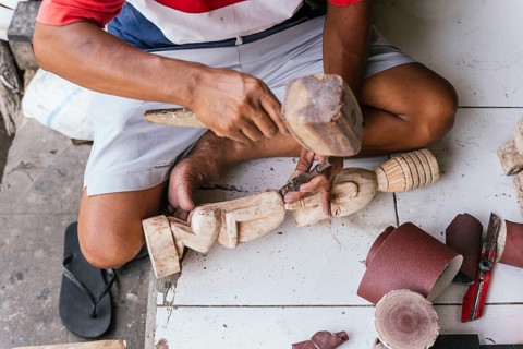 Indonesian man skillfully carves a wooden sculpture, highlighting traditional craftsmanship. Ethnic