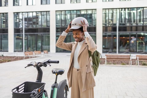 Black woman wearing a stylish outfit prepares for an urban bike ride, adjusting her helmet The