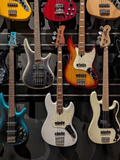 A collection of electric bass guitars in diverse colors arranged on a wall display. The sleek,