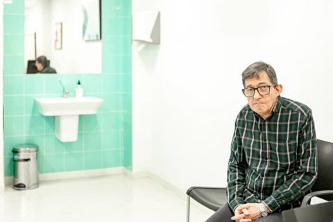 Man with glasses sits in a mental health facility, waiting for his appointment. The clinical