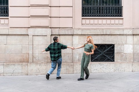 A joyful Colombian lesbian couple dances hand in hand in an urban setting, celebrating love and