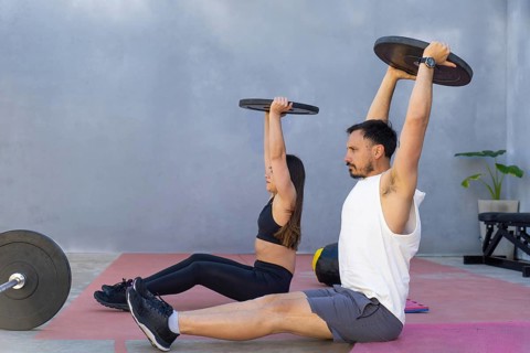 Two fitness professionals are performing a core strengthening exercise, lifting weights while