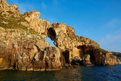 A large rock formation with a natural arc over the sea, morning light, Tsichli Babas islet,