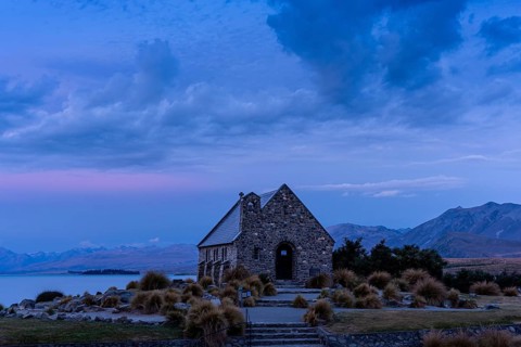 The small church The Church of the Good Shepherd on Lake Tekapo with a cloudy sky at sunset.