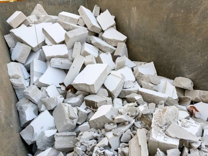 A large container is filled with construction waste from broken white porous concrete or gypsum