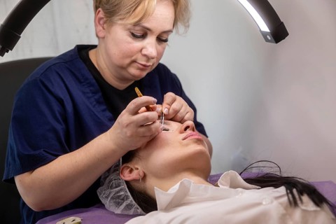 A beauty professional meticulously applies eyelash extensions in a salon setting. The scene