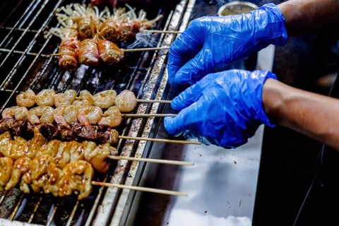 Close-up of a cropped unrecognizable food vendor preparing assorted meats on skewers at a bustling