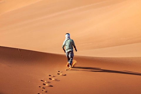 Person walks alone over sand dunes, leaves footprints in the golden desert sand, Tuareg walks