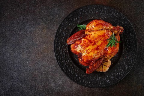 Baked chicken on a black dish with herbs and garlic, on a dark background, homemade, no people
