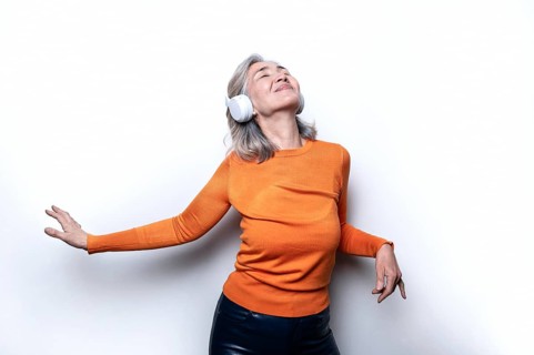 Asian Chinese senior woman wearing headphones and an orange sweater, enjoying music with a joyful