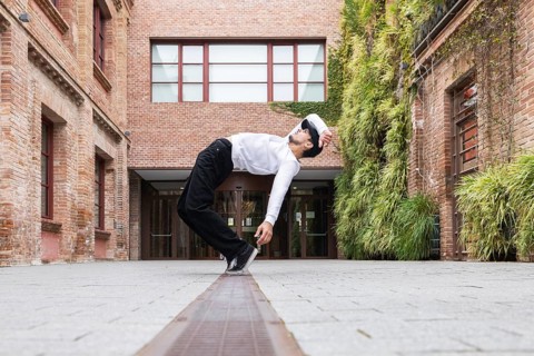 A cuban man in a white shirt and black pants dances dynamically in an urban outdoor area with brick