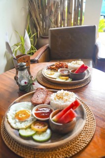 Two plates of filipino breakfast featuring rice, fried egg, meat, vegetables, watermelon, and