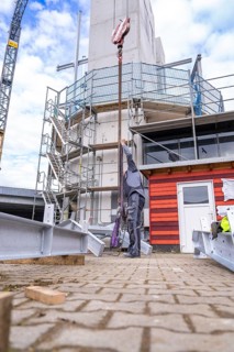 Construction worker pulling a heavy object up a building with a crane, stairway extension to the