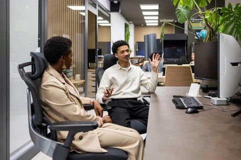 Colleagues engage in a lively discussion at a modern office desk, surrounded by computers and