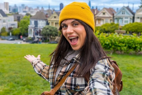 Excited young woman in a yellow beanie and plaid jacket making a selfie, inviting viewers to