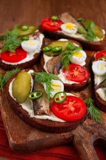 Sandwiches on rye bread with sprats, quail eggs, fresh tomatoes and pickled cucumber, on a wooden