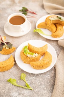 Homemade salted crescent-shaped cheese cookies, cup of coffee on brown concrete background and