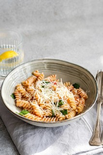 A ceramic bowl filled with cavatappi pasta topped with cheese, fresh spinach and spicy tomato sauce