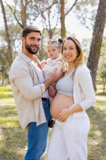 A joyful pregnant woman with her family, including a man and a young child, enjoying time outside