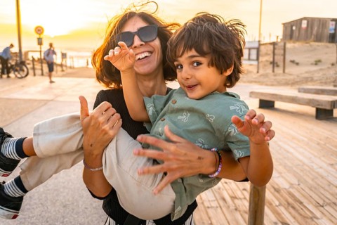Happy mother holding her young son, both smiling and having fun outdoors on a wooden boardwalk at
