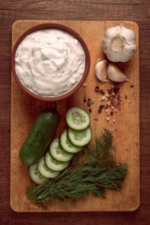 Greek zajiki sauce, in a clay bowl, on a wooden board, with ingredients, top view, no people