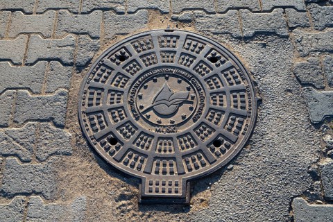 A detailed manhole cover with exemplary structures on an asphalted road, Fethiye, Mugla, Aegean