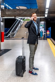 Young businessman talking on phone while waiting for subway train, holding reusable coffee cup and