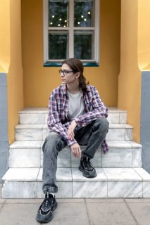 A teenage boy with long hair and glasses sits pensively on marble steps outside a brightly painted