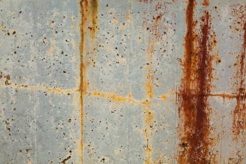 Close-up of long brownish rust streaks, yellow orange stains and small holes on old light greyish