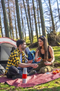 Couple enjoying a relaxing camping trip, playing cards near their tent amidst the serene beauty of