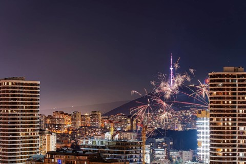 Vibrant fireworks illuminate the night sky over downtown Tbilisi, Georgia, with skyscrapers in the