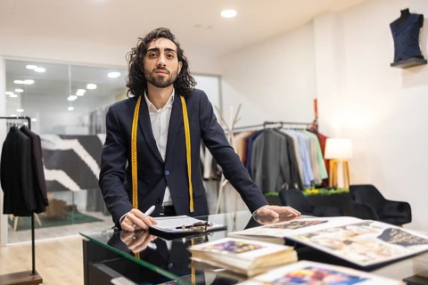 A professional tailor in a sleek boutique leans on a glass table surrounded by measuring tape and