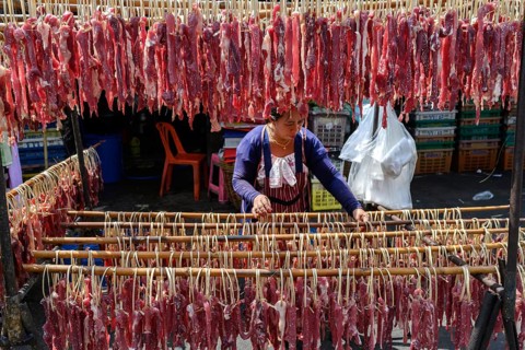 Bangkok, Thailand. February 19th 2025. A Thai woman hangs salted meat to dry in the sun at the