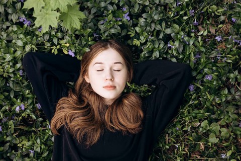 A serene teenage girl lies peacefully among lush vegetation and periwinkle flowers in a tranquil