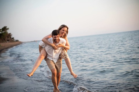 A joyful couple enjoys a playful day at an Italian beach, with one partner giving the other a