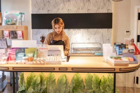 Female employee stands behind the counter of a cosmetics store, surrounded by beauty products. The