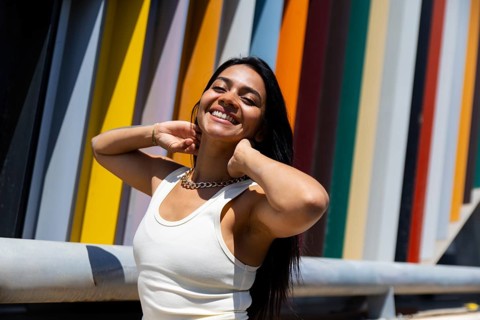 A woman in a vibrant outfit poses against modern architectural elements. The colorful backdrop