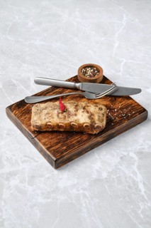 Juicy grilled ribs on a rustic wooden board, with a small bowl of mixed spices. A knife and fork