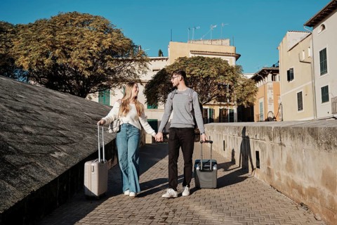 A young couple walks hand in hand with suitcases, exploring the charming streets of Majorca, Spain,